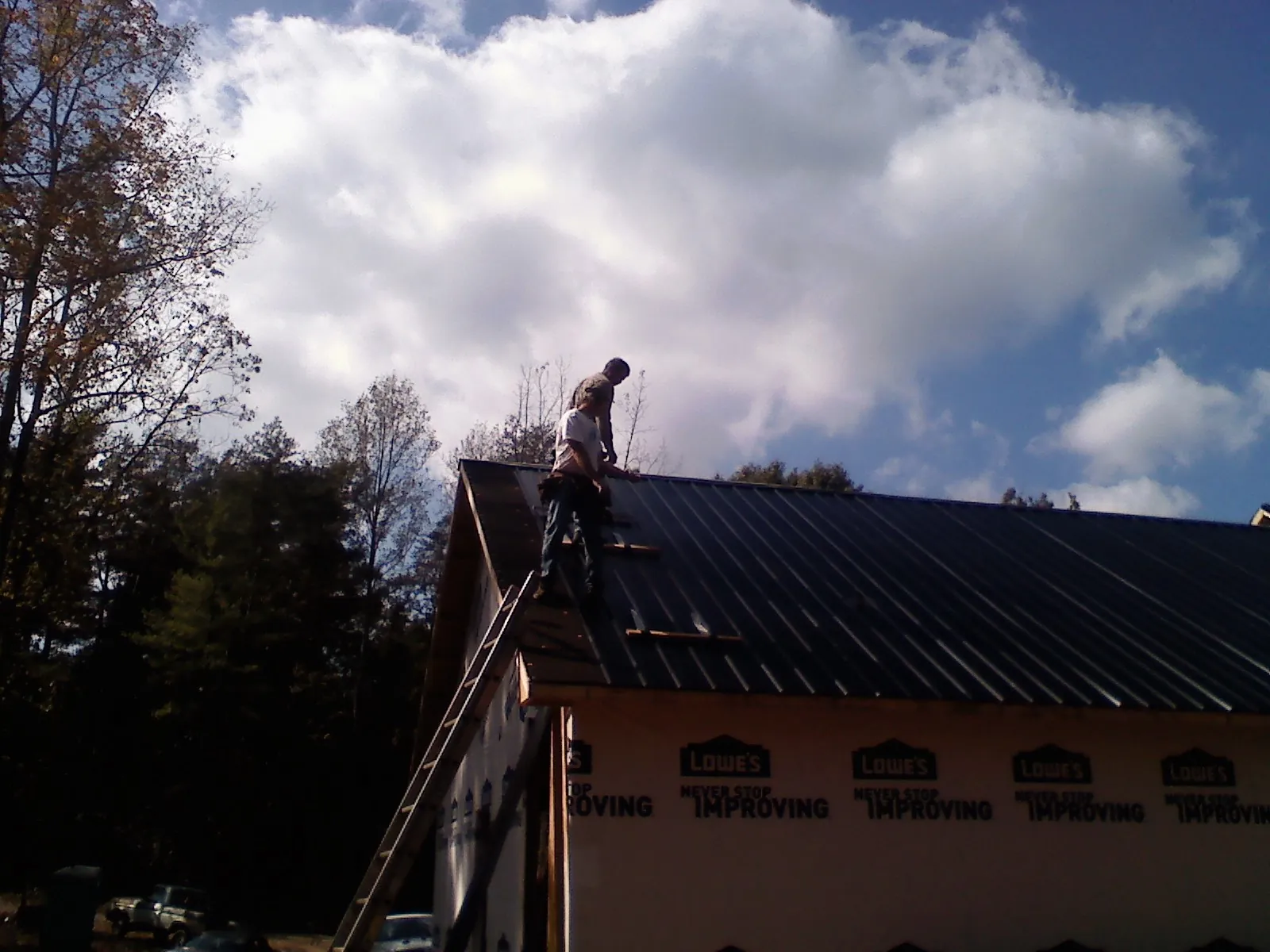 Roofer fastening dark metal panels high against a cloudy sky, from a Roof Inspection job in Colonial Beach
