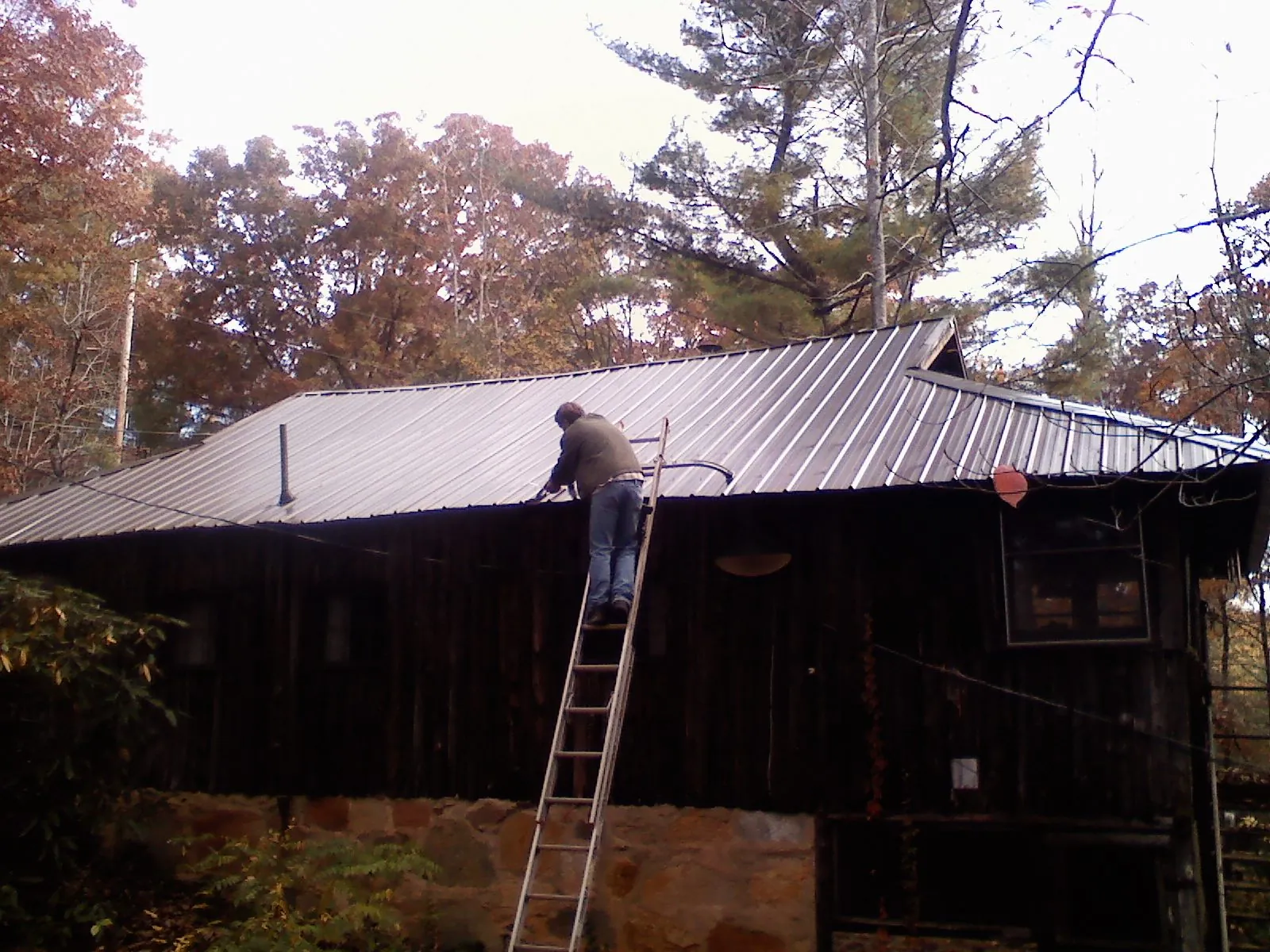 Roofer on a ladder working along the edge of a cabin metal roof in Colonial Beach