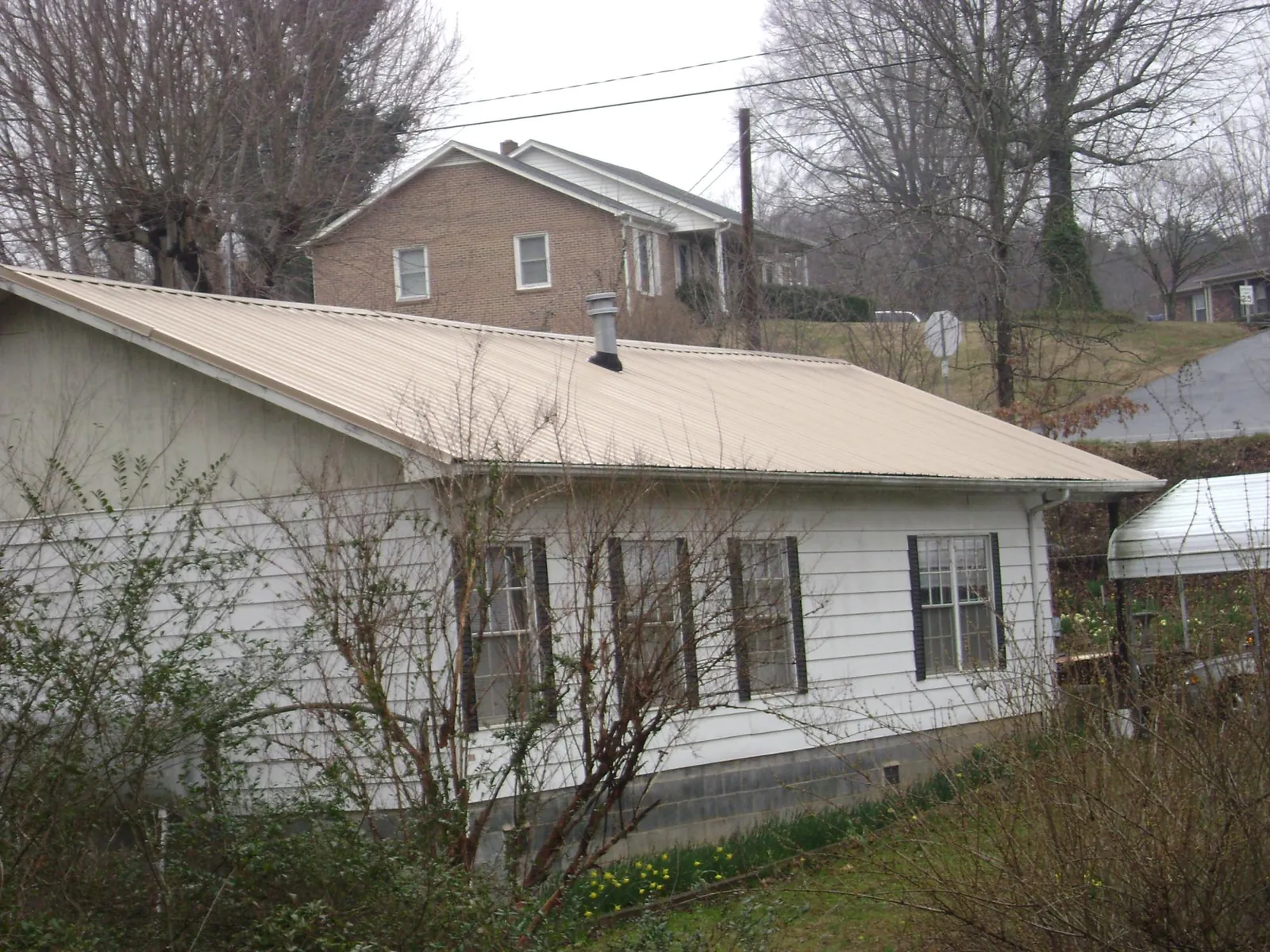 Tan metal roof on a white sided house set into a hillside — Commercial Roofing by Roofing Brothers in Colonial Beach